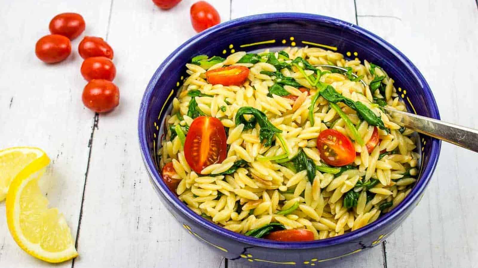 Creamy spinach orzo in a blue bowl with tomatoes nearby.