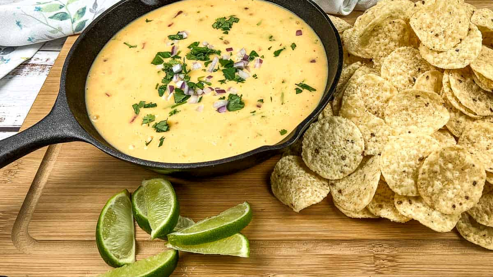 Velveeta queso in a skillet with tortilla chips and lime wedges.
