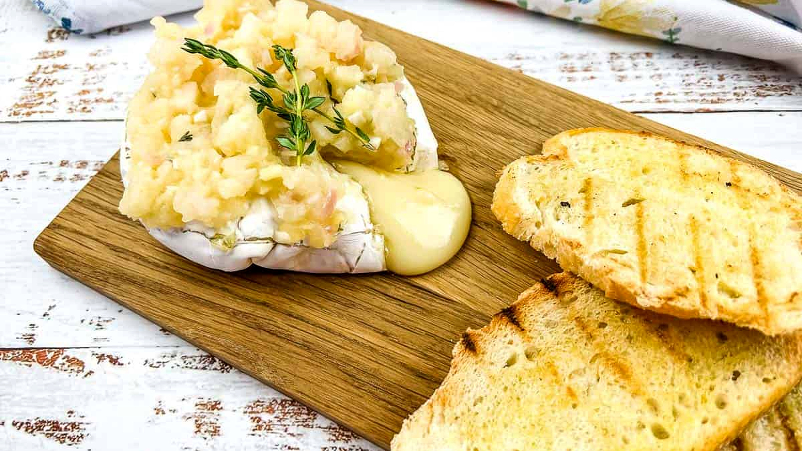 A chunk of oozing brie with apple chutney on a board.