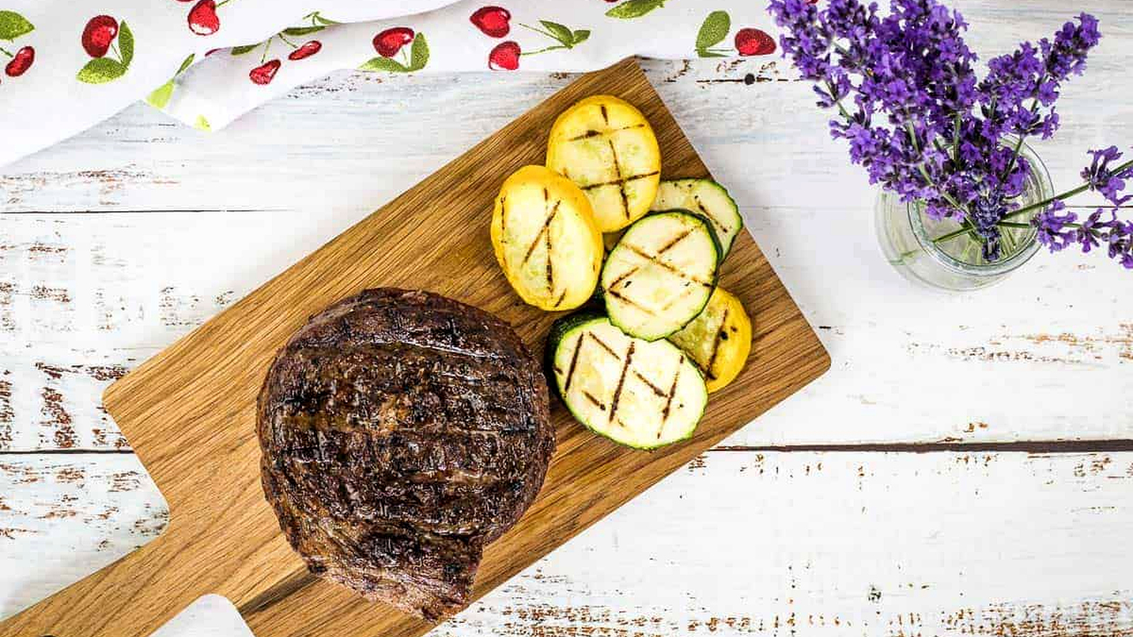 A top-down shot of Grilled Ribeye Cap Steak on a cutting board with veggies.