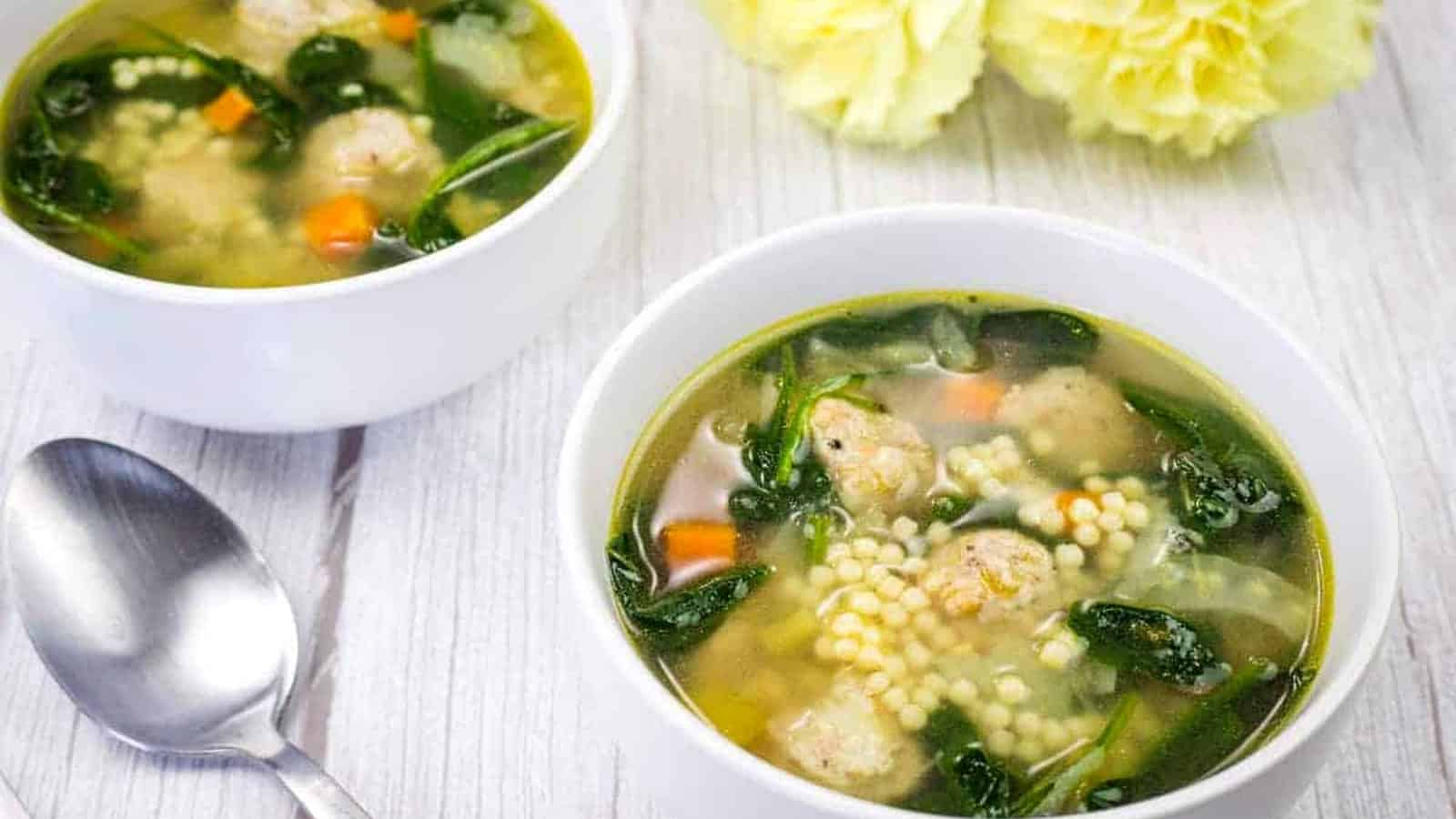 Two bowls of Italian soup accompanied by yellow flowers and a spoon.