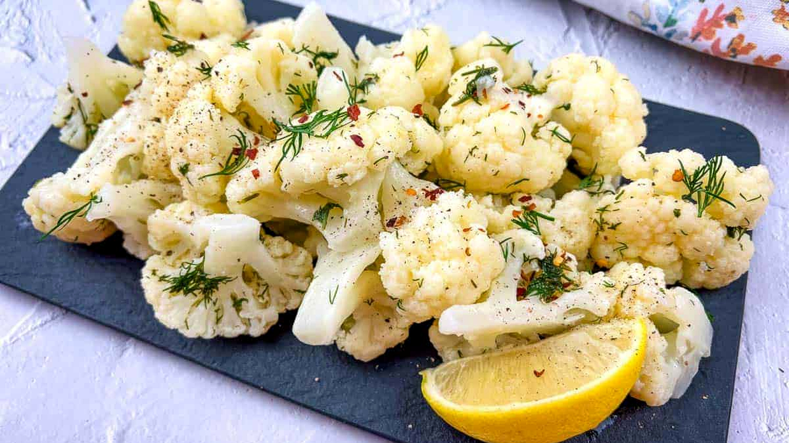 Cauliflower with lemon and dill on a black board.