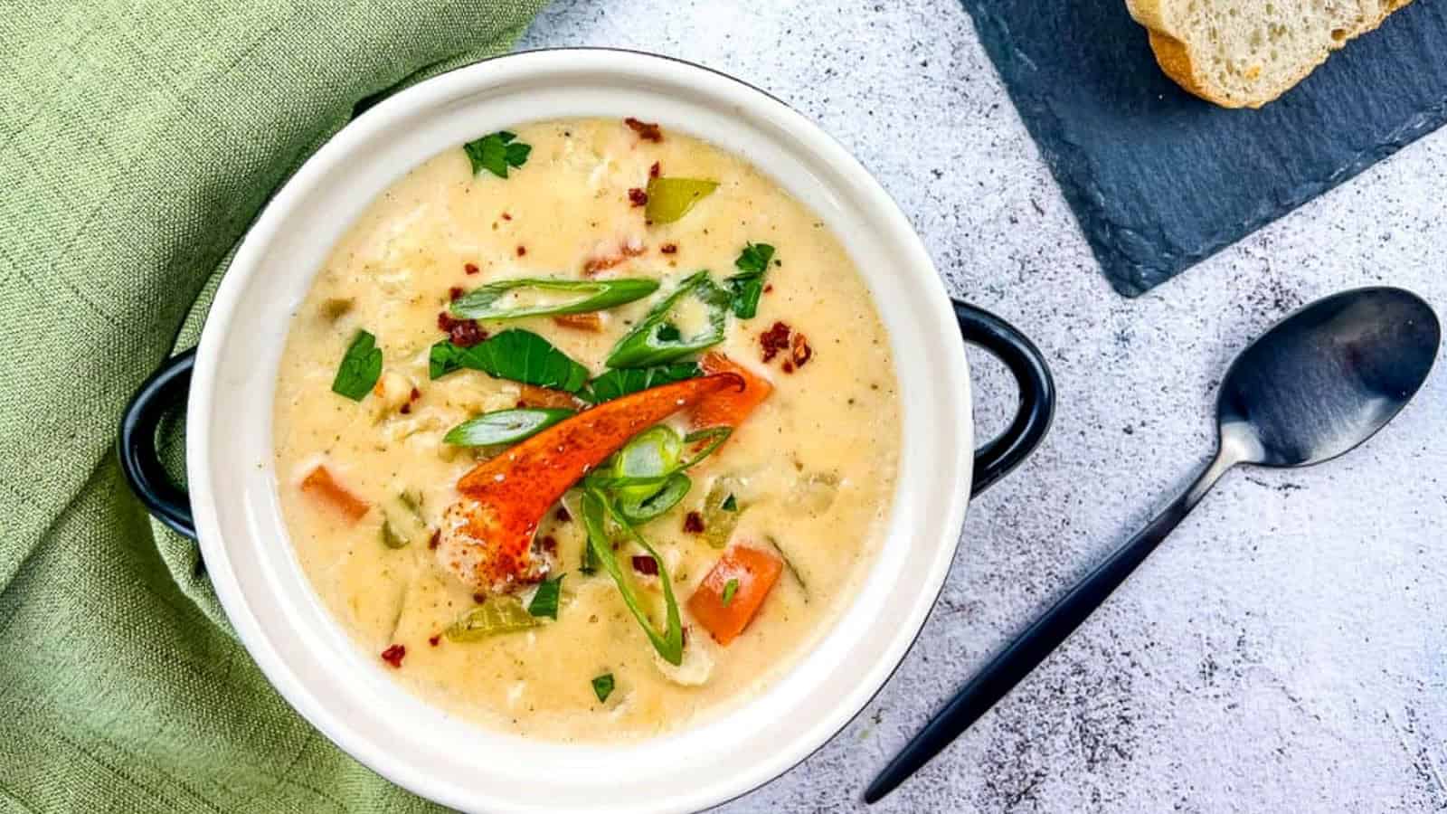 A bowl of lobster chowder with bread on the side.