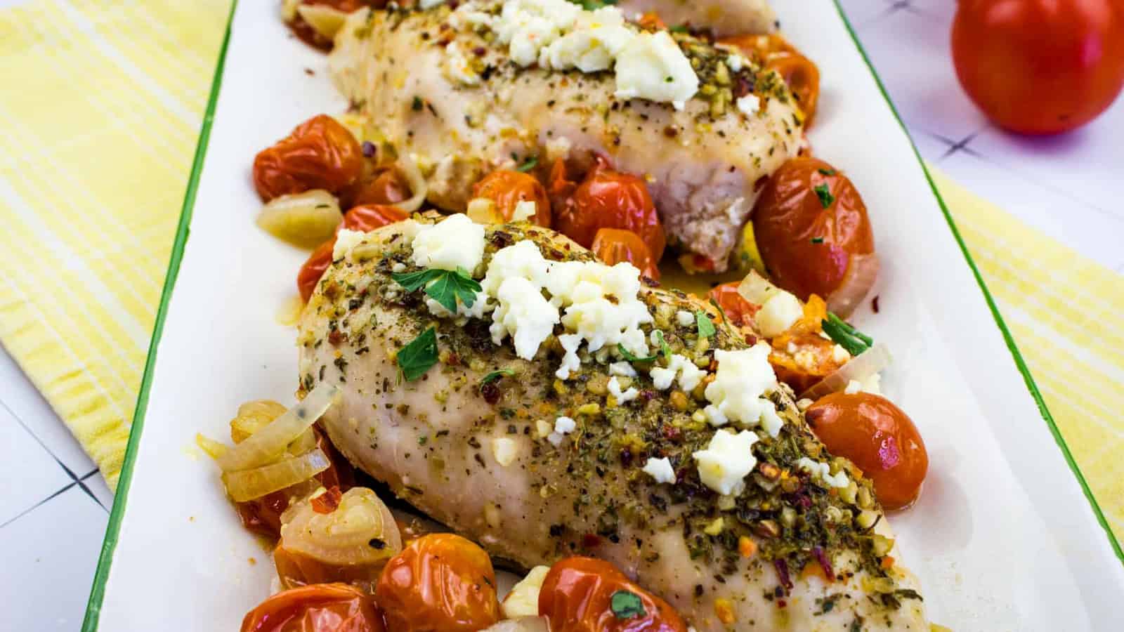Mediterranean Chicken Bake with herbs, cheese and tomatoes in a platter.