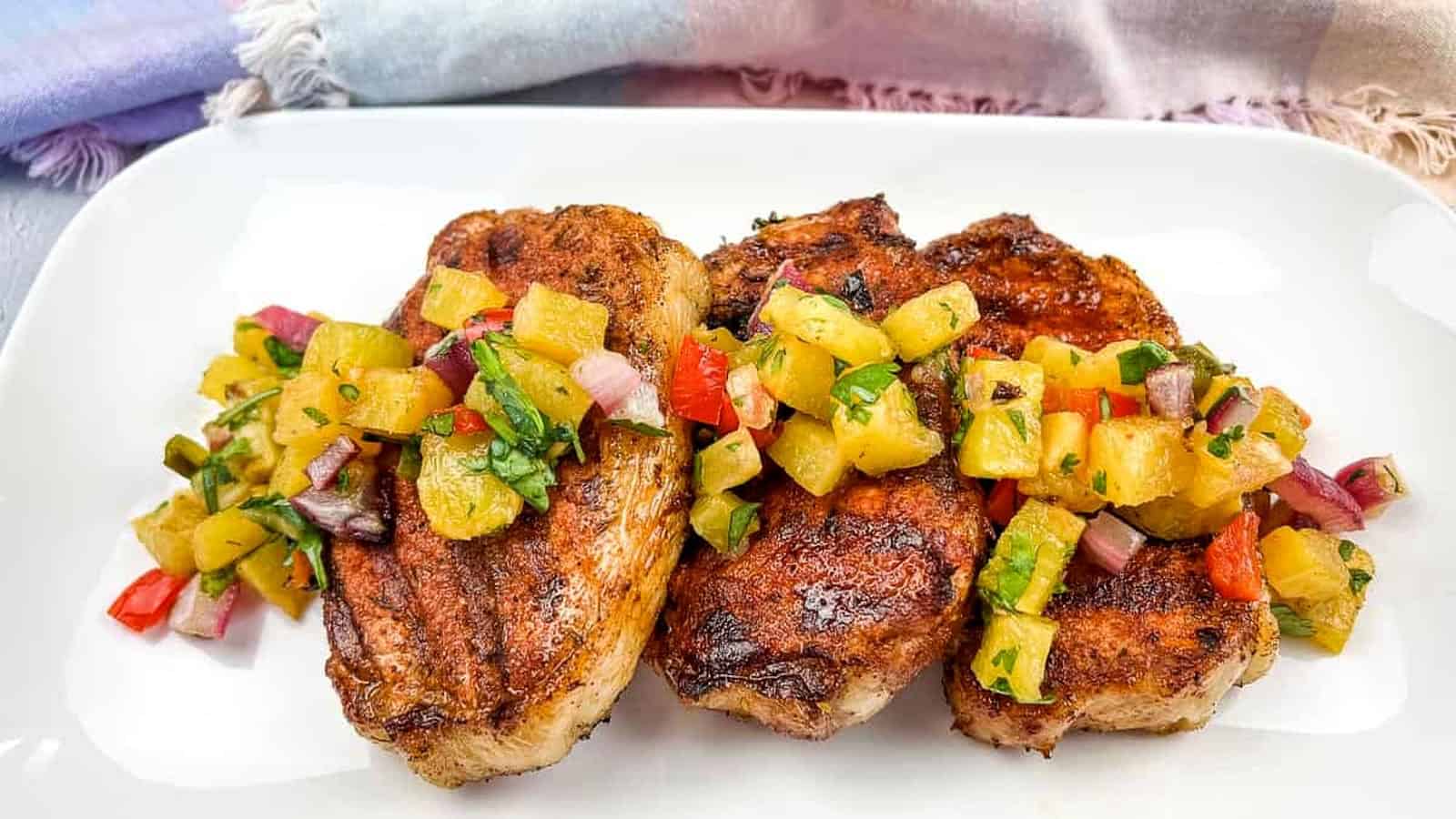 Grilled pork chops with pineapple salsa on a white plate.