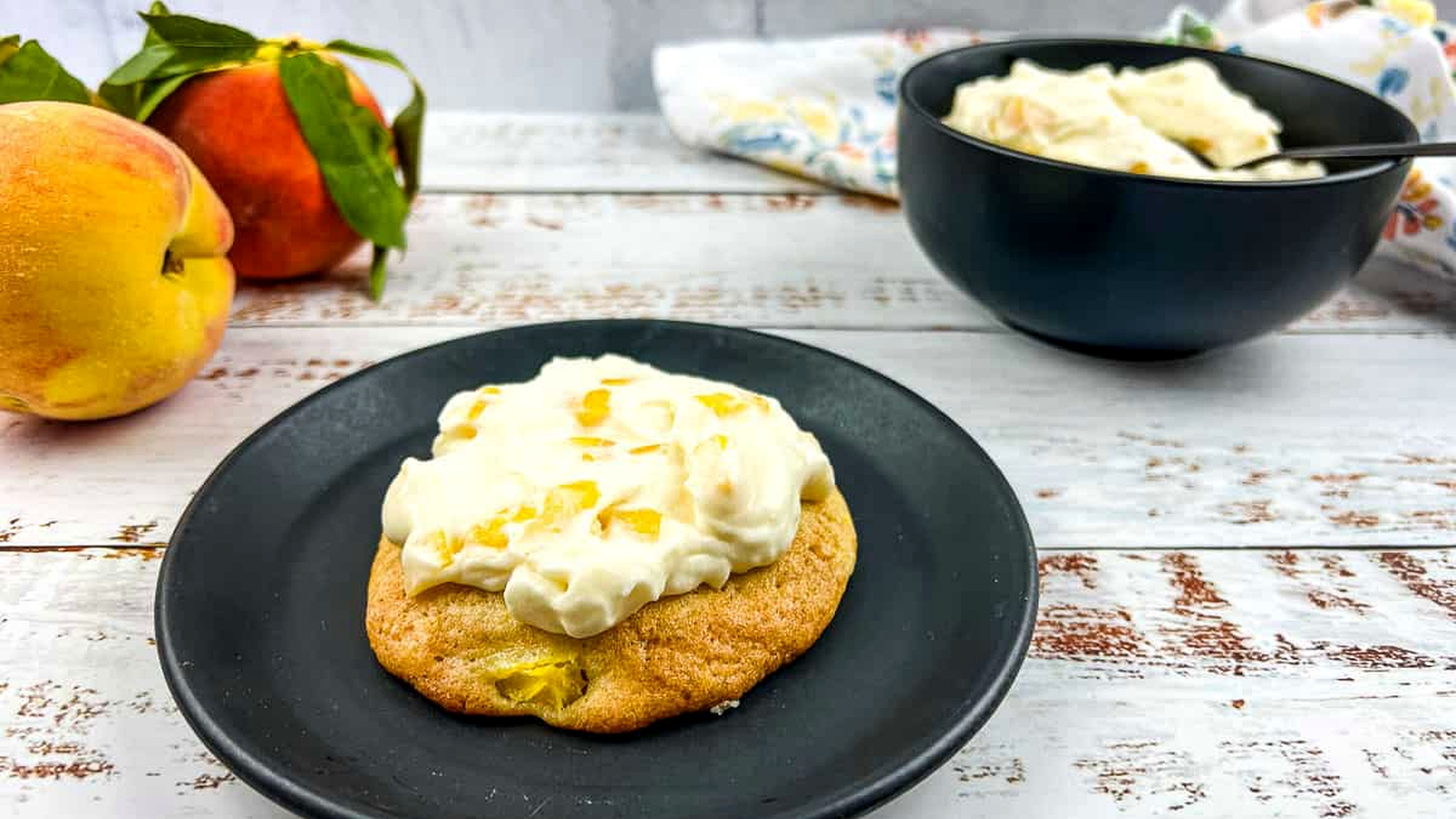 Peaches and cream cookies on a plate with fresh peaches nearby.