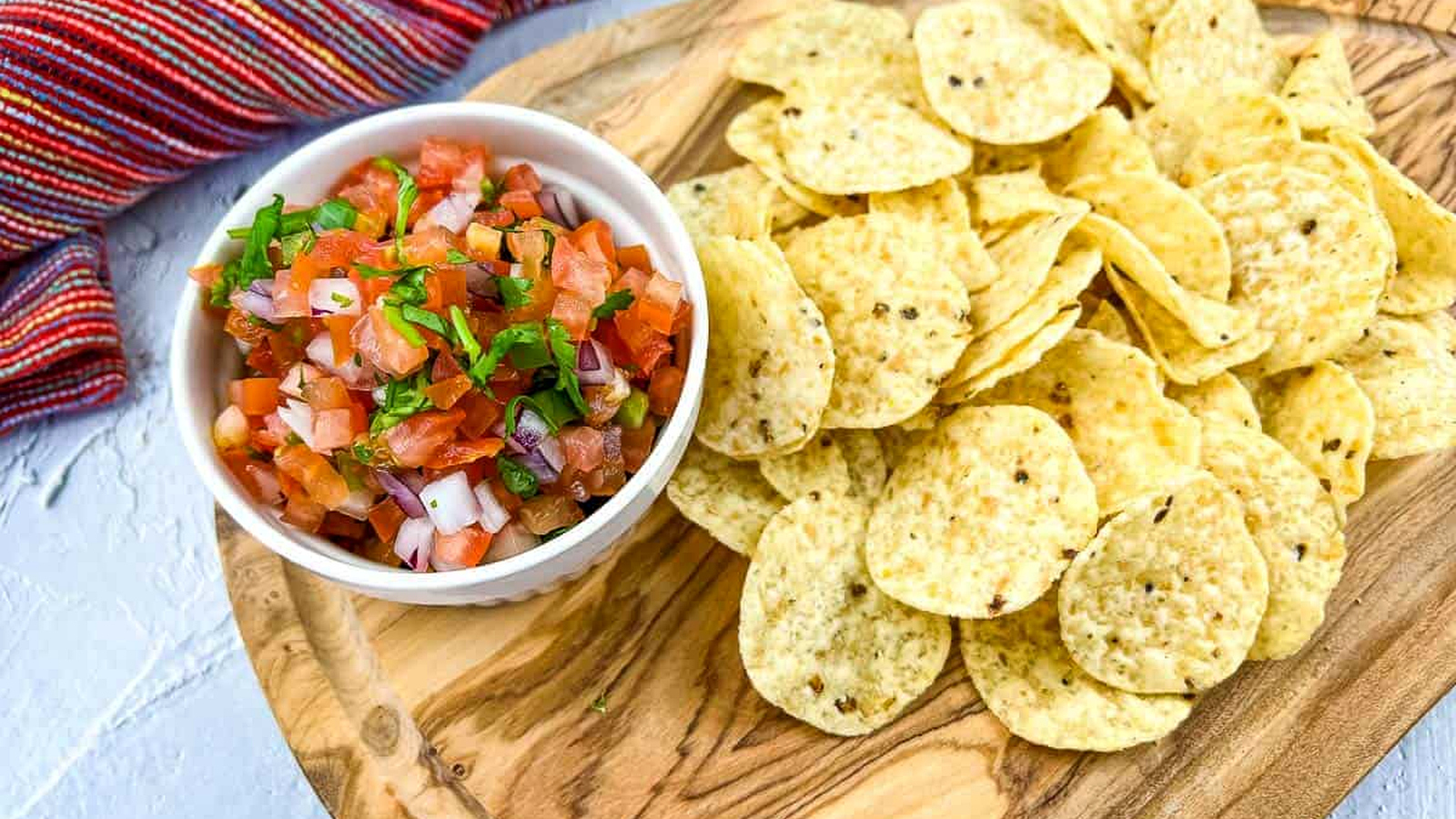 A shot of Pico de Gallo on a board with chips nearby.