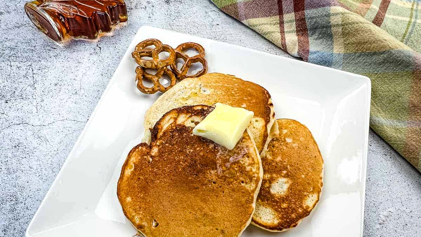 Pretzel pancakes with a bottle of maple syrup nearby.