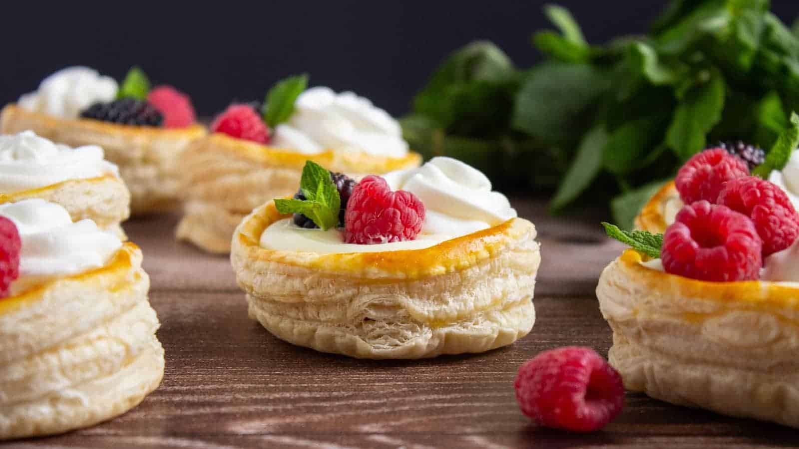 Puff pastry shells filled with cream, topped with fresh raspberries, blackberries, and mint leaves, arranged on a wooden surface.