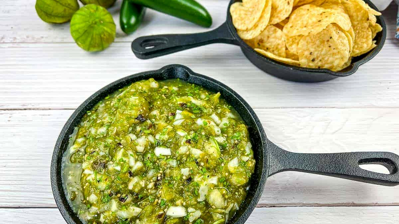 Roasted Tomatillo Salsa in a black pan with tortilla chips in a second pan.