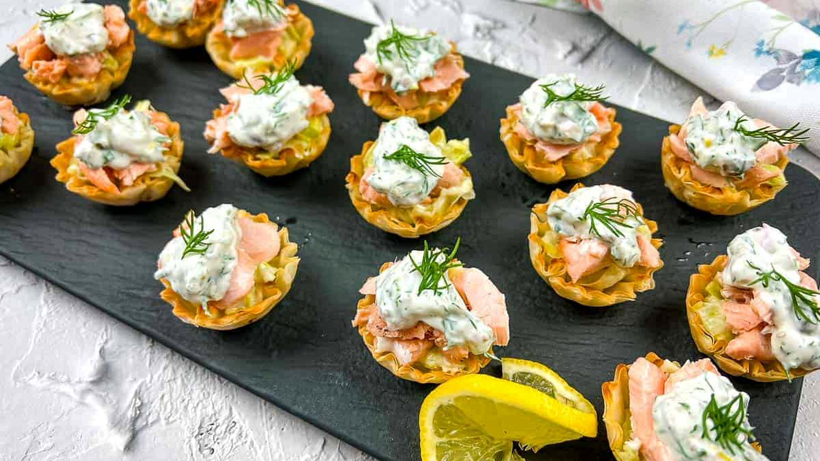 Salmon & Leek Phyllo Tartlets with lemon wedges on a black plate.