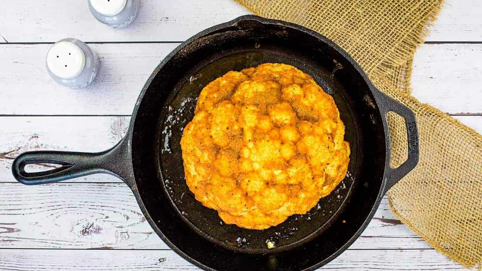 Smoked cauliflower in a skillet on a wooden table.