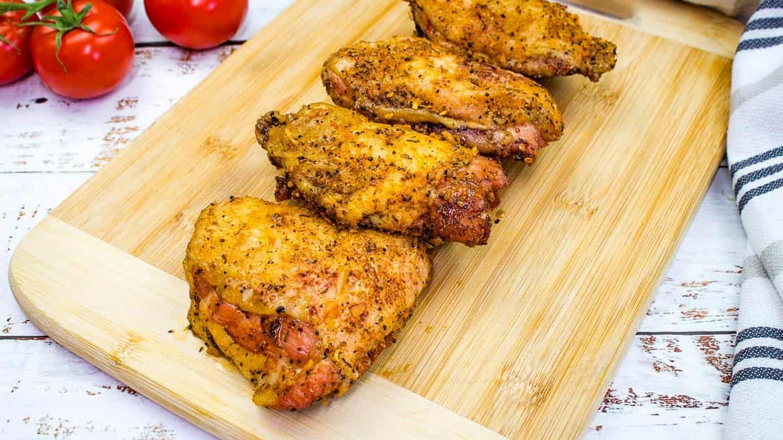 Chicken thighs on a cutting board with tomatoes.