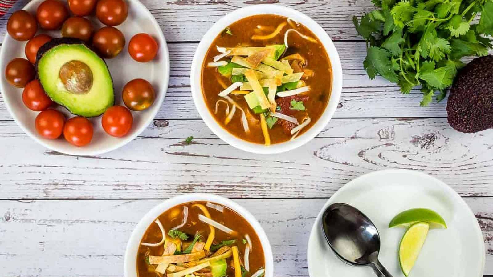 Smoked Chicken Tortilla Soup in two white bowls with garnishes nearby.