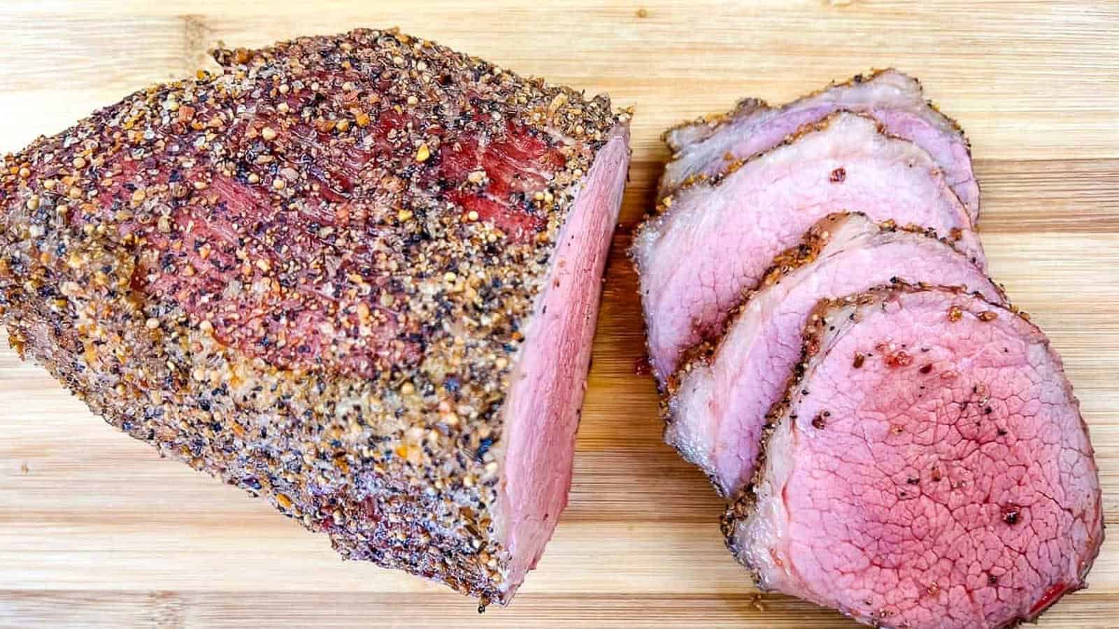 A whole and sliced smoked eye of round with on a wooden cutting board.