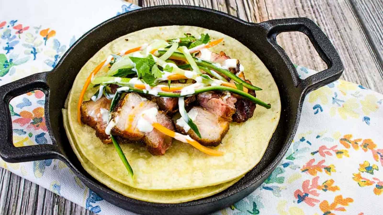 A closeup shot of two tacos filled with smoked pork belly and vegetables.
