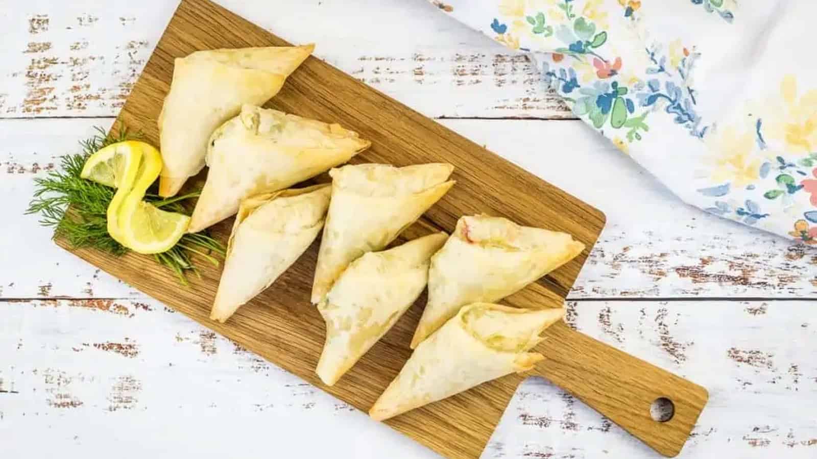 Crab Spanakopita triangles on a cutting board.
