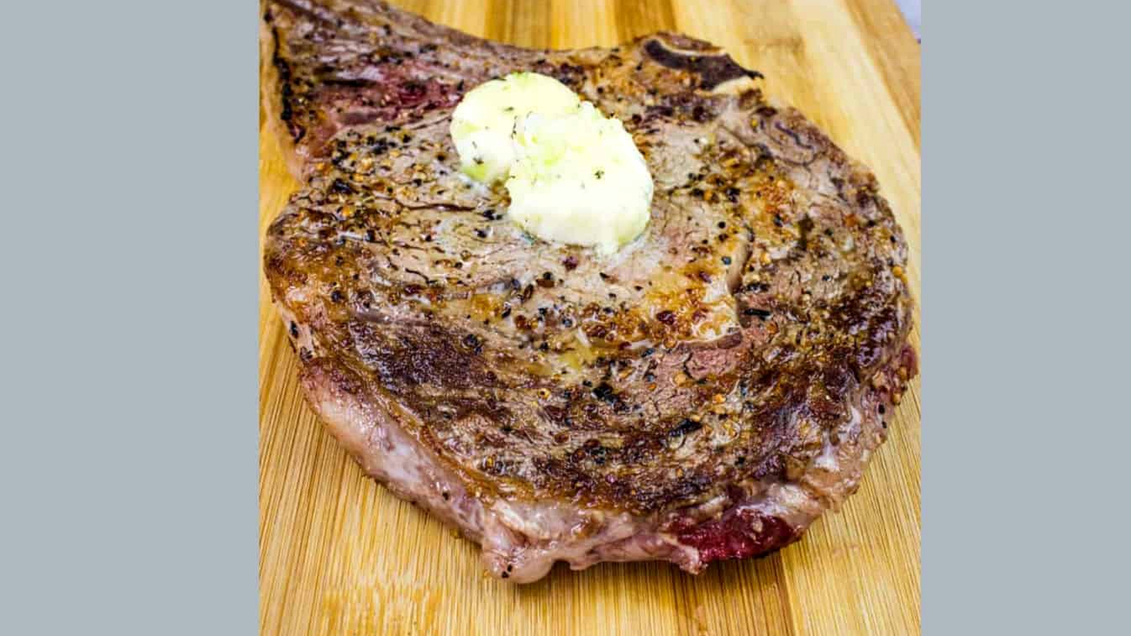 A steak on a cutting board with butter on it.