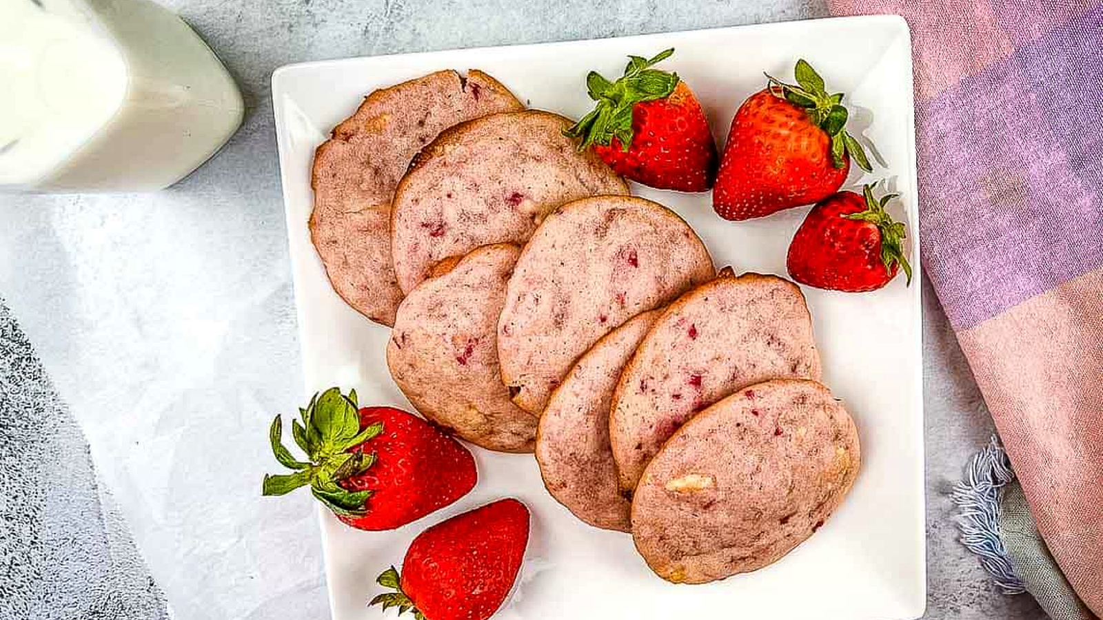 Strawberry Shortcake Cookies on a white plate with strawberries nearby.
