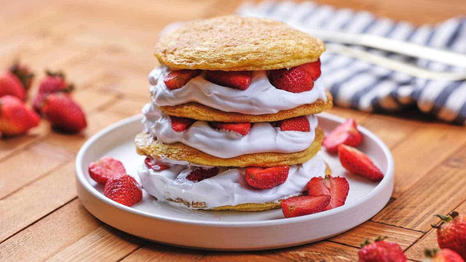 A stack of strawberry shortcake pancakes on white stand with toothpick and mint leaves.