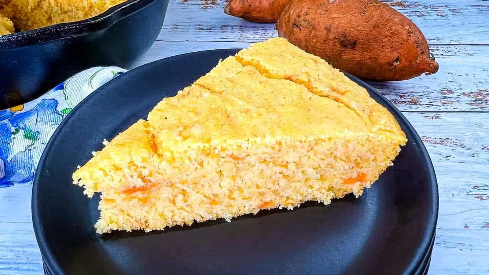 A piece of cornbread on a plate next to a few potatoes.