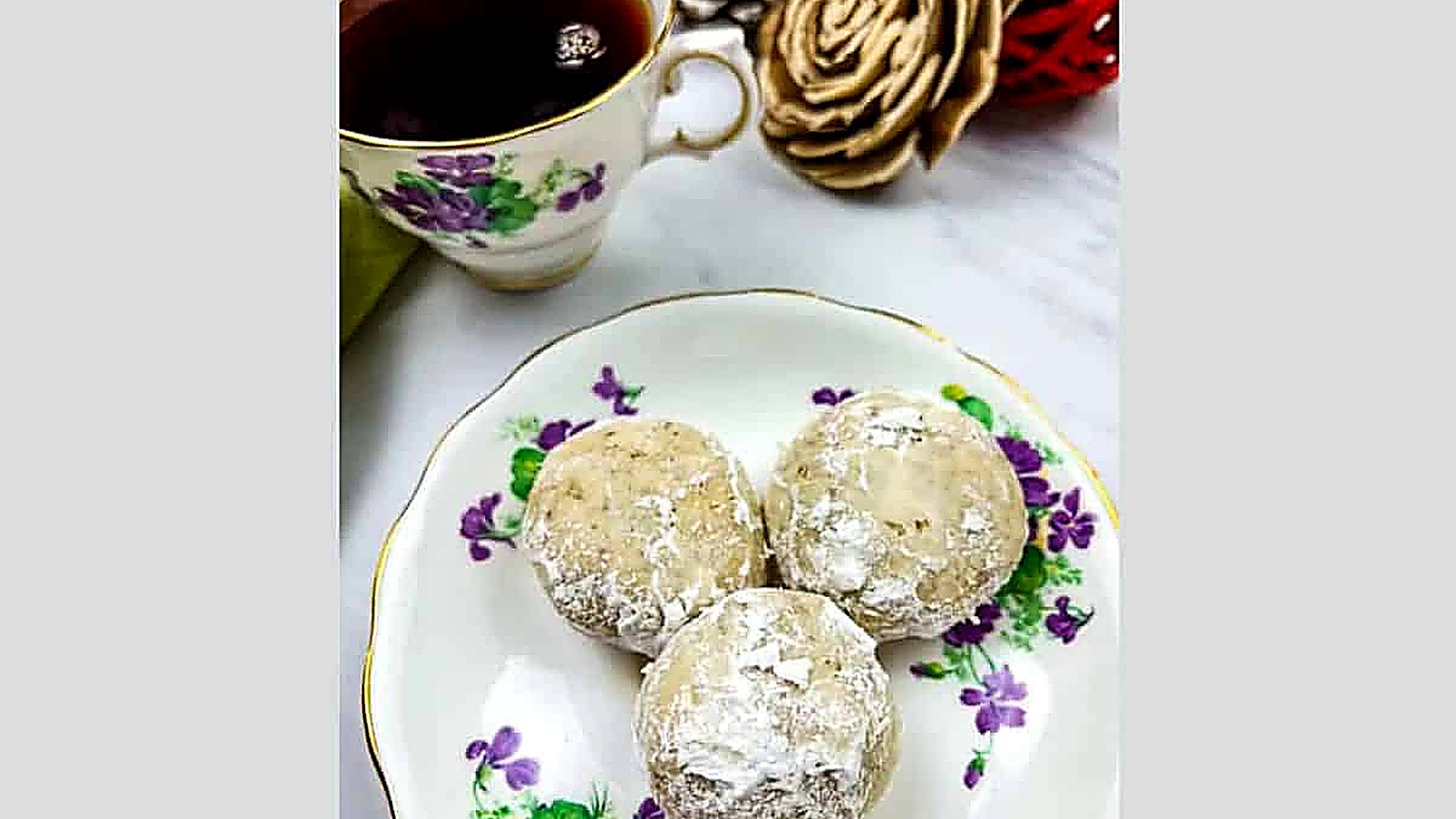 Top-down shot of seven pecan butter balls on a black plate.