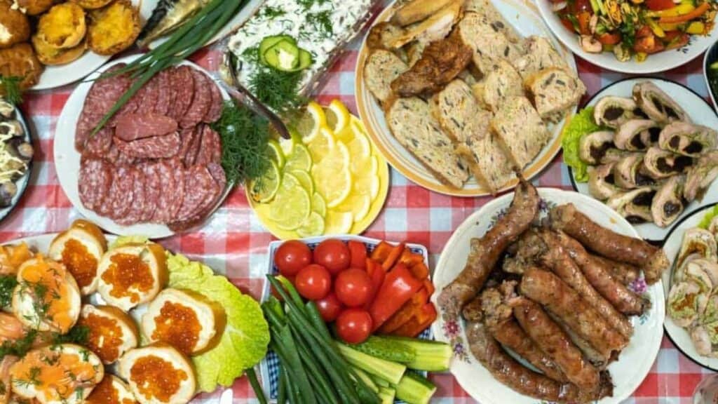 A table covered with assorted meats, sausages, sliced salami, stuffed eggs, vegetables, bread, and garnishes on a red and white checkered tablecloth&mdash;perfectly arranged in accordance with traditional potluck rules.