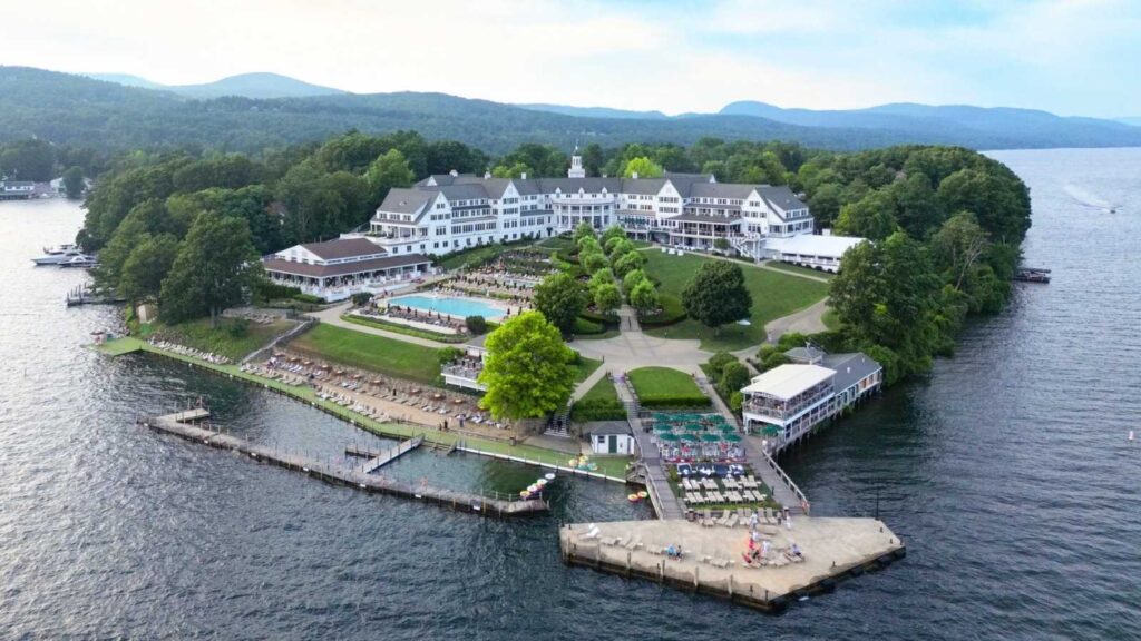 A large lakeside resort with multiple buildings, a pool, walking paths, and docks, surrounded by trees and water, seen from above.