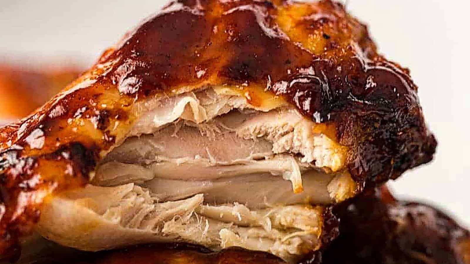 Close-up of a cooked chicken wing with a bite taken, showing juicy and tender meat covered in dark barbecue sauce.