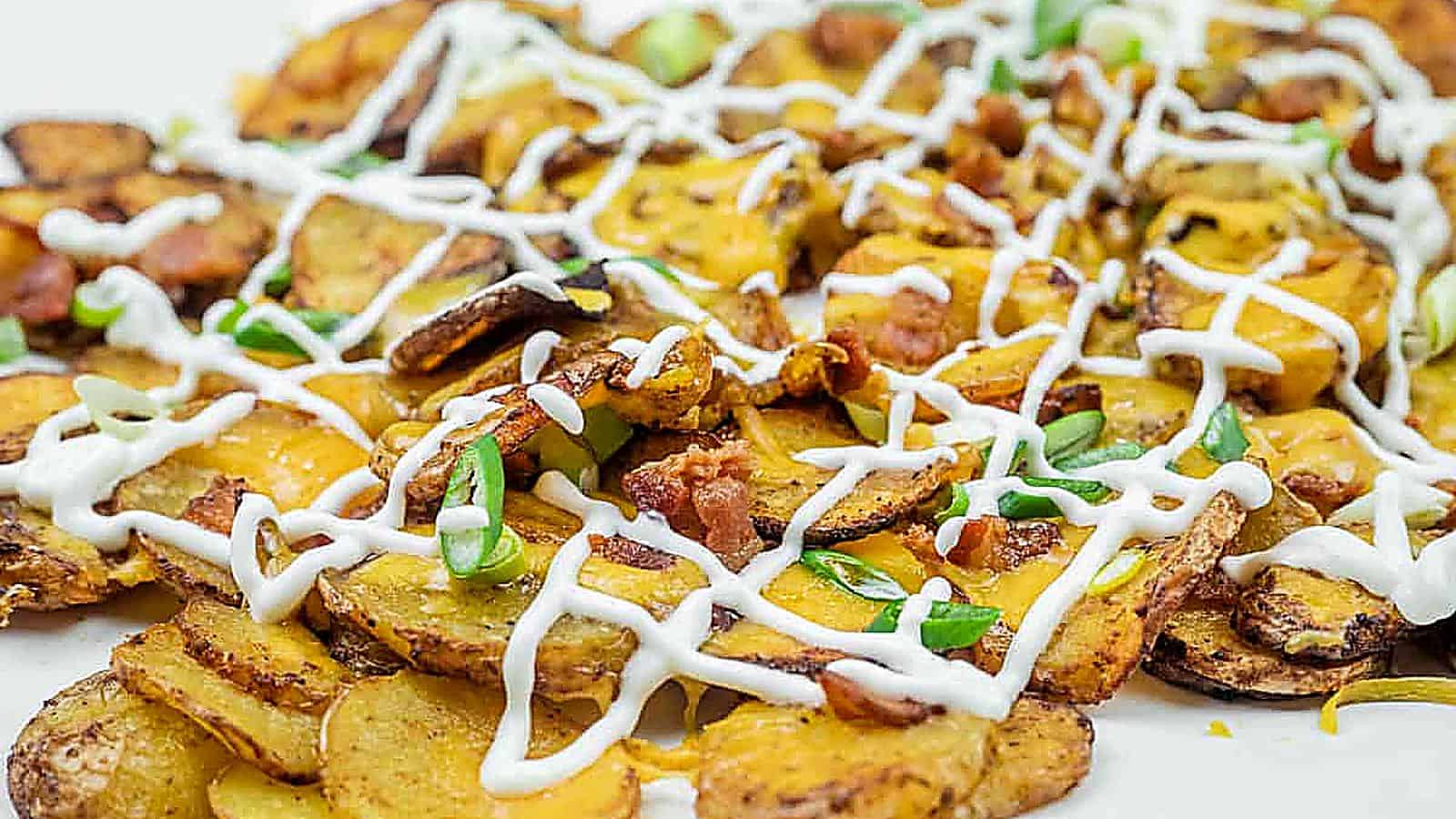 A platter of Air Fryer Irish Nachos topped with melted cheese, sour cream, bacon bits, and chopped green onions.
