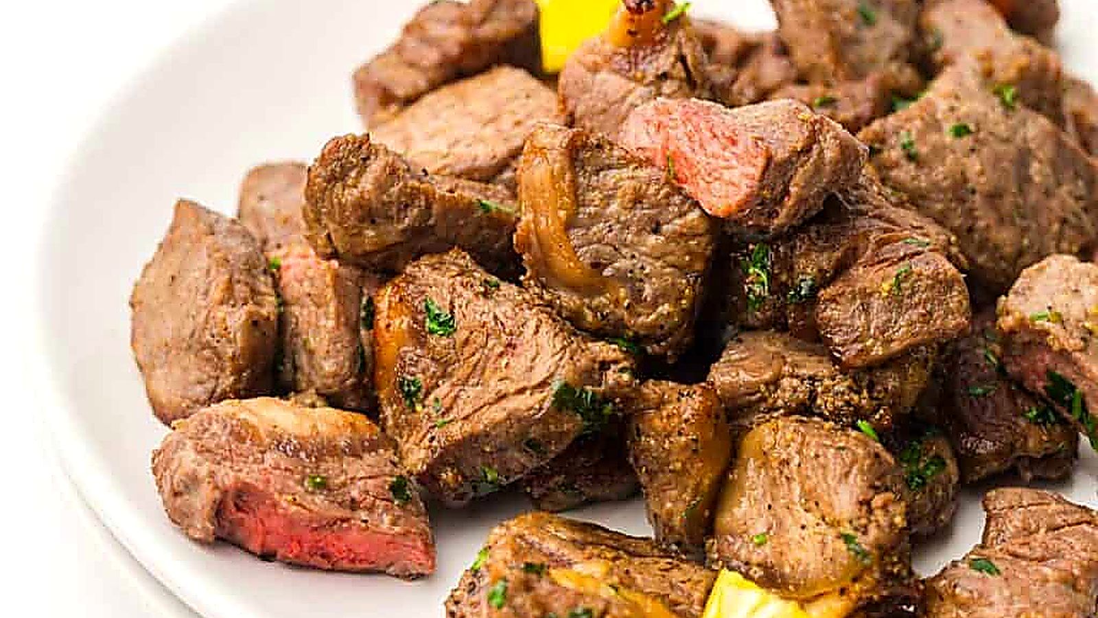 A plate of cooked steak bites garnished with herbs, served with pieces of yellow bell pepper.
