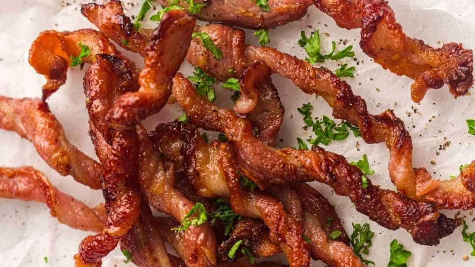 Crispy twisted strips of cooked bacon garnished with chopped parsley, displayed on a white surface.