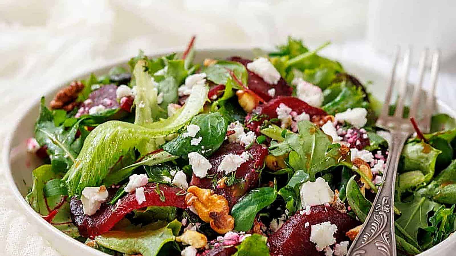 A Beet Salad with Goat Cheese and Walnuts in a white bowl, accompanied by a fork.