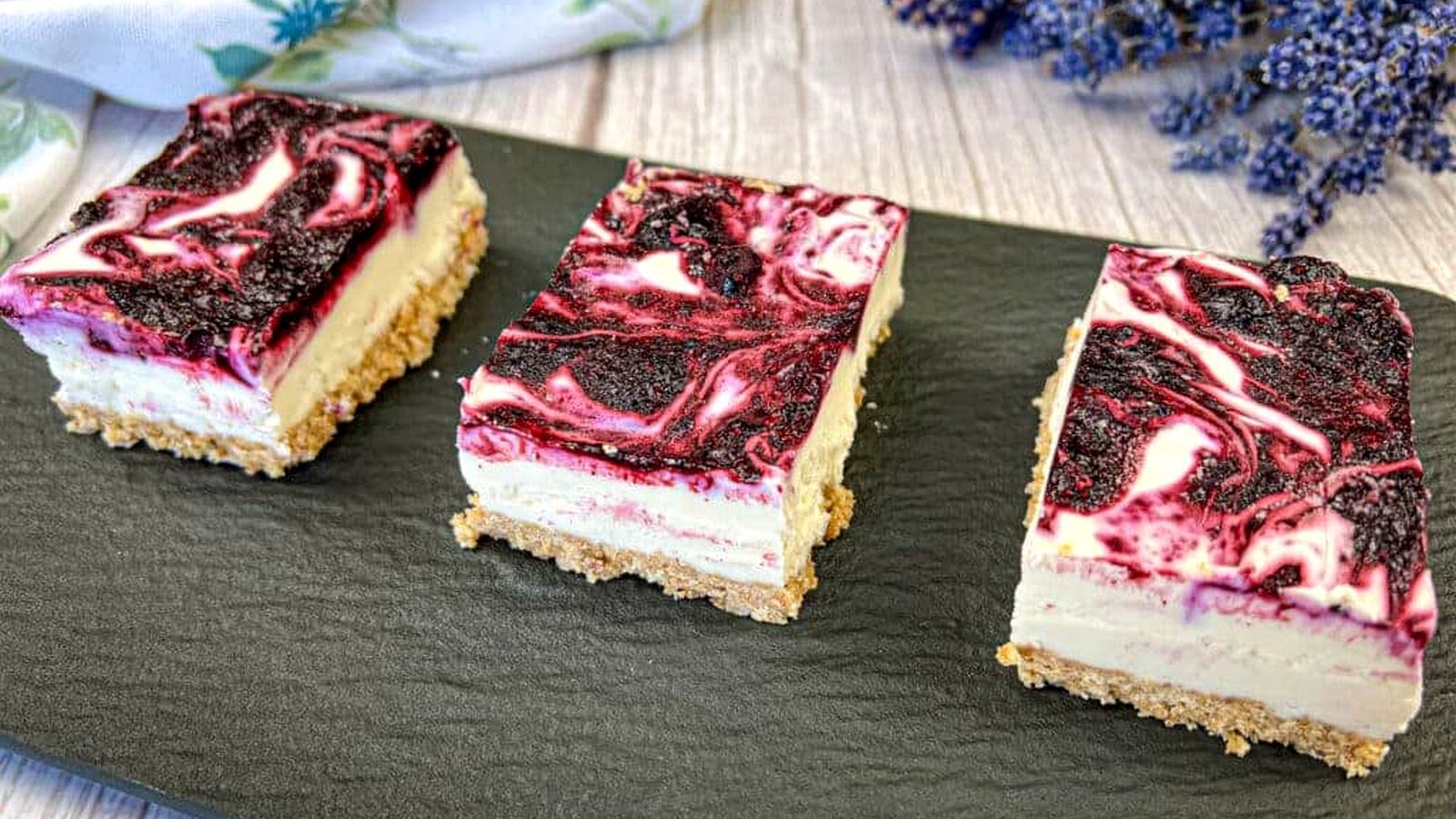 Three slices of Blueberry Cheesecake Bars on a rectangular black slate.