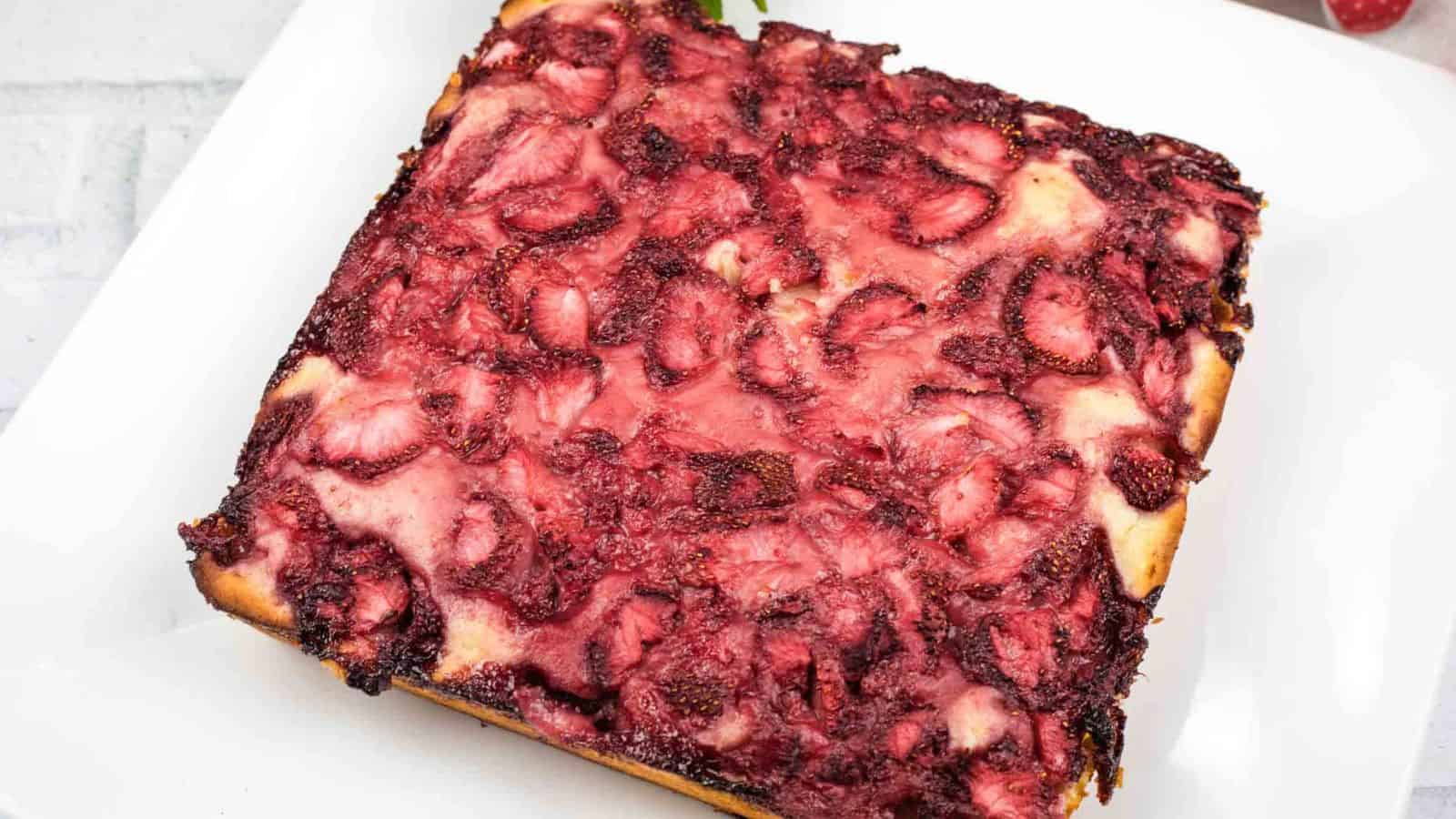 Square piece of cake with a baked strawberry topping on a white plate.
