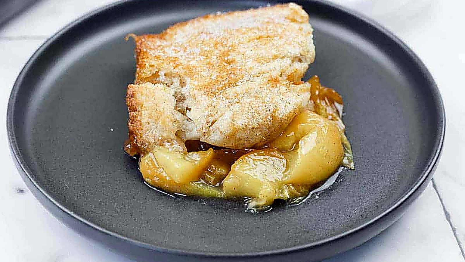 A serving of peach cobbler with a golden crust and peach filling on a black plate.