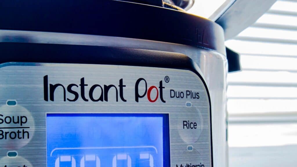 Close-up of an Instant Pot Duo Plus electric pressure cooker and slow cooker, showing its digital display and part of the control panel with buttons for Soup, Broth, and Rice.