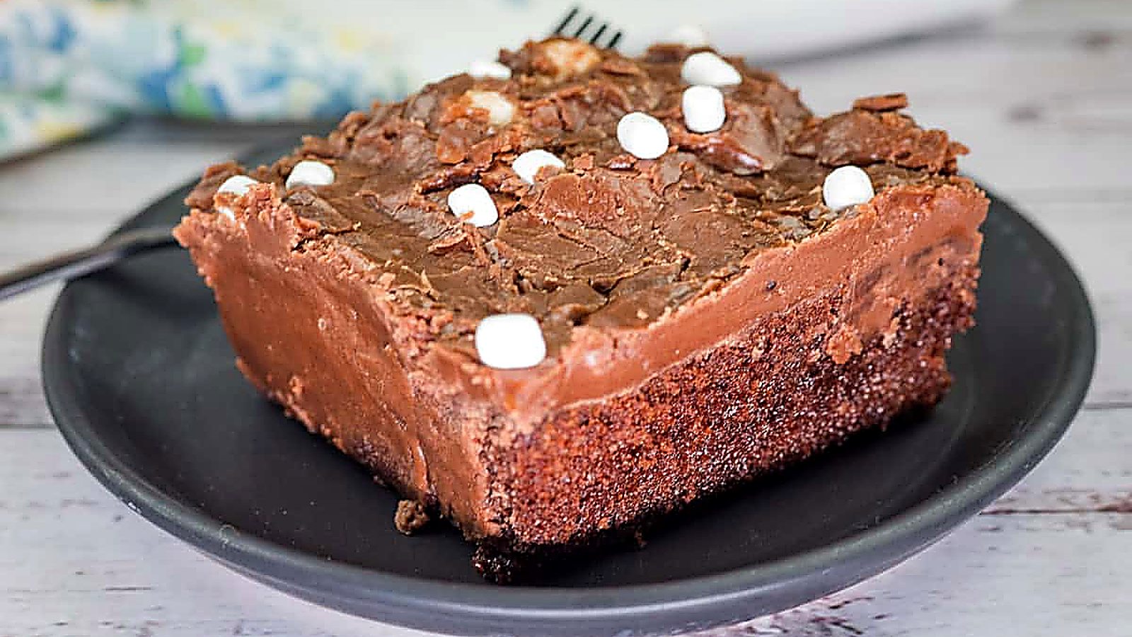 A slice of Grandma's Coca-Cola cake with chocolate frosting and small marshmallows on a black plate.