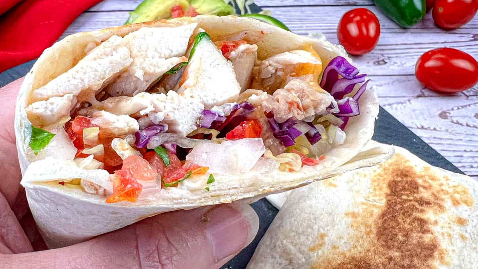 A close-up of a hand holding a copycat Taco Bell Cantina chicken burrito.