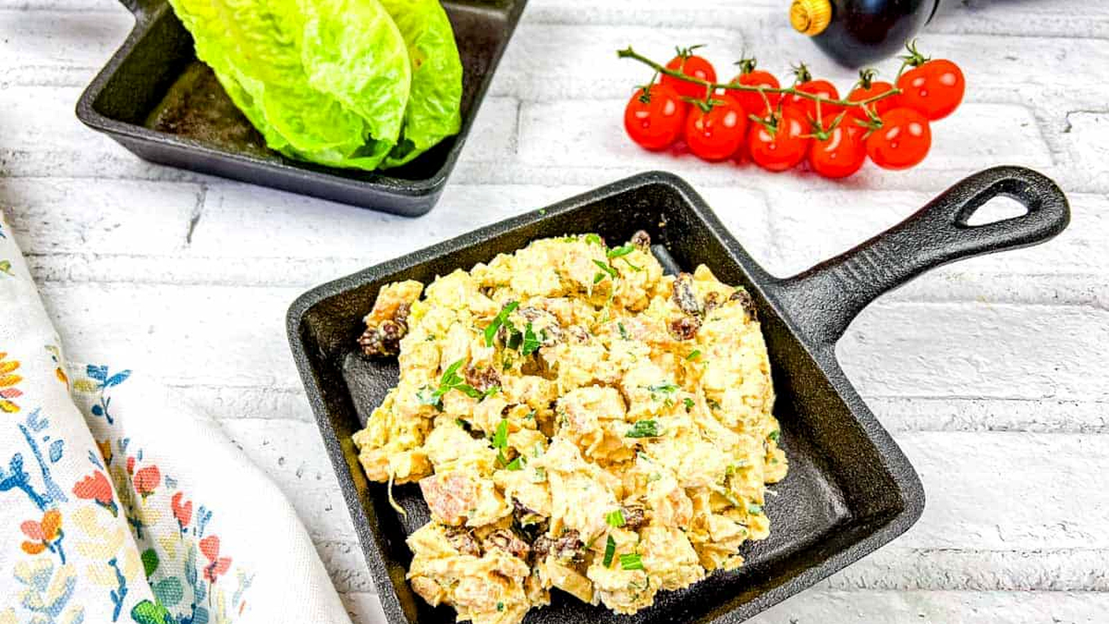 A pan of coronation chicken salad next to a plate of lettuce and tomatoes.