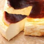 A Basque burnt cheesecake with a dark, caramelized top sits on parchment paper, its rich and creamy texture making it a standout choice on cheesecake menus, with one slice slightly separated from the rest of the cake.