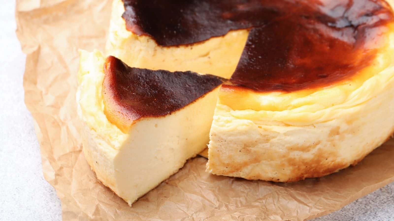 A Basque burnt cheesecake with a dark, caramelized top sits on parchment paper, its rich and creamy texture making it a standout choice on cheesecake menus, with one slice slightly separated from the rest of the cake.