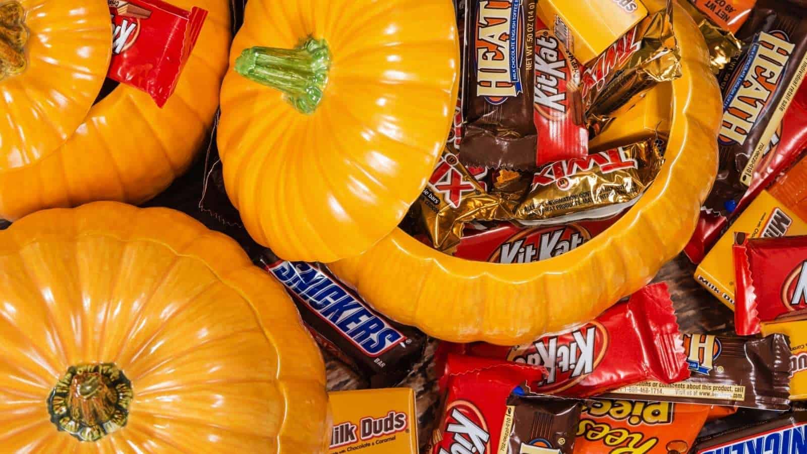 Yellow pumpkin containers filled with assorted chocolate and candy bars such as Kit Kat, Snickers, Milk Duds, and Heath. The photo suggests a Halloween or autumn theme.