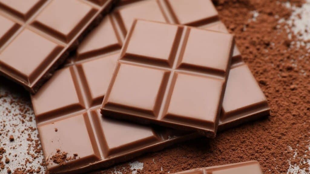 Several pieces of milk chocolate are stacked on a surface dusted with cocoa powder.