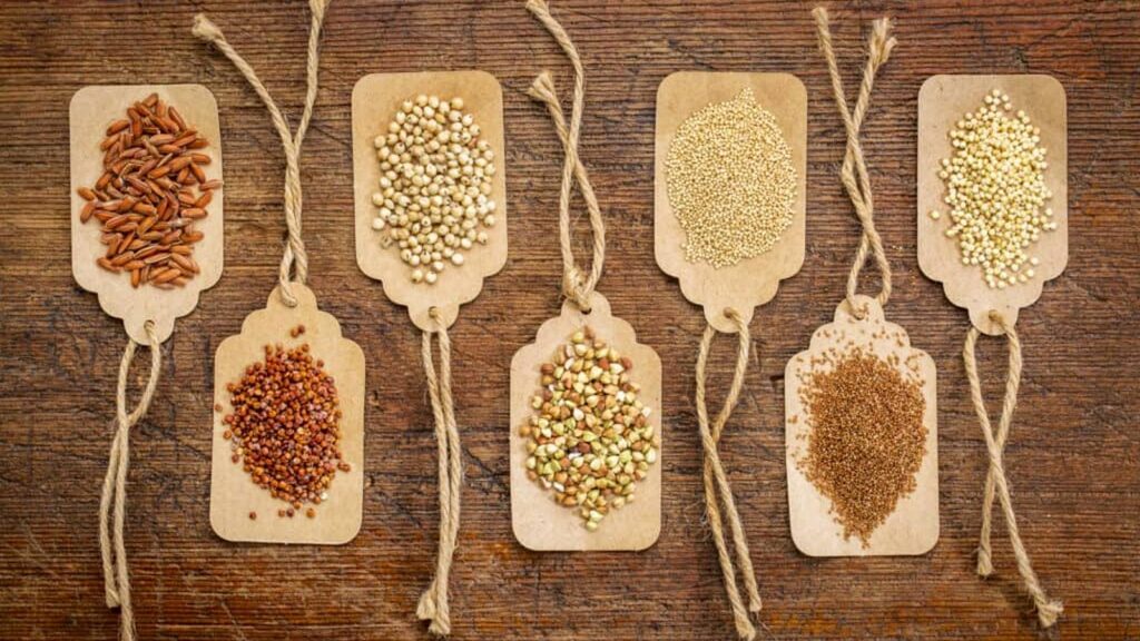 Seven types of grains are displayed on brown tags with twine, arranged in a row on a wooden surface.
