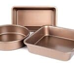 Three nonstick baking pans in different shapes—one rectangle, one round, and one square—are elegantly displayed on a white background.