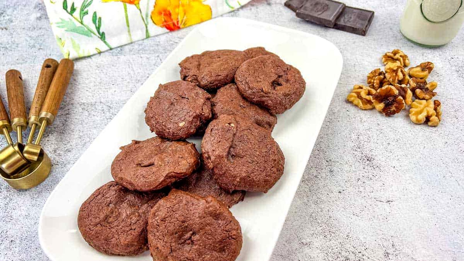 A plate of chocolate cookies with walnuts and chocolate pieces on the side.