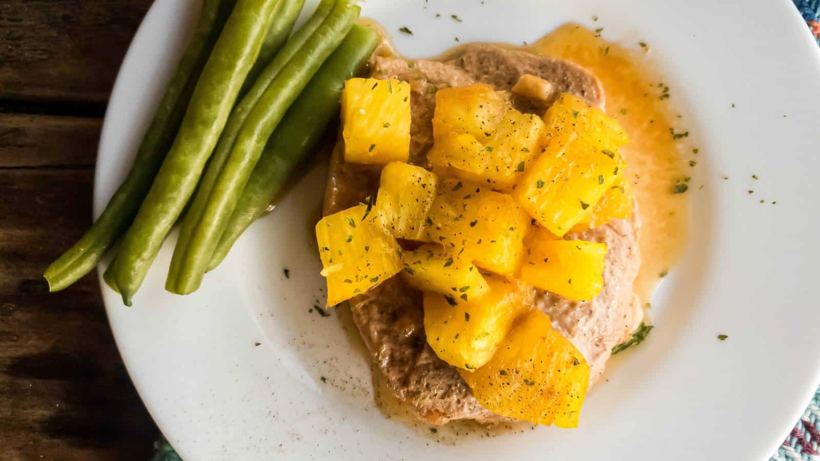 Oven baked pork chop with pineapple and green beans, white plate wooden background.