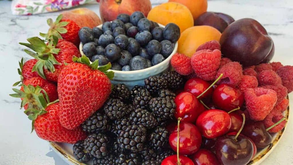 A plate of assorted fresh fruits including strawberries, blackberries, blueberries, cherries, raspberries, peaches, apricots, and plums.