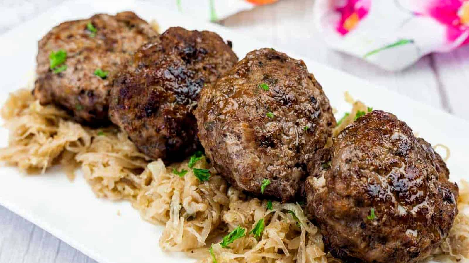 Four browned meat patties are served on a bed of shredded cooked cabbage on a white rectangular plate.